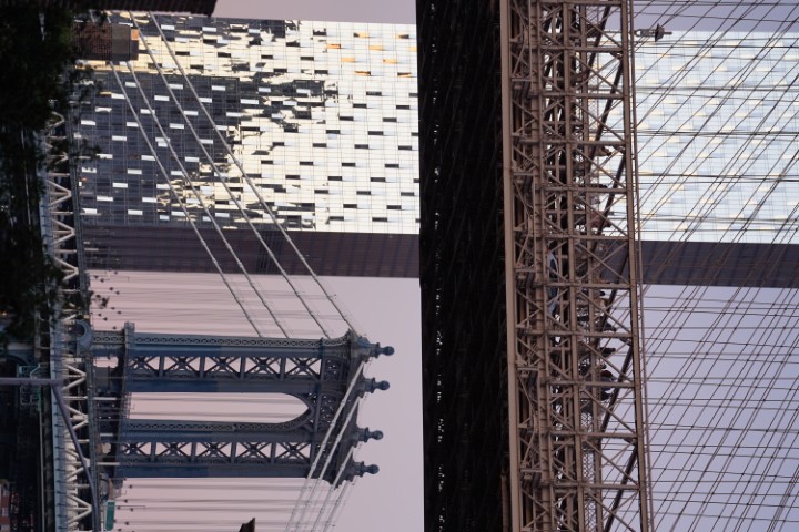 A cropped-out view of a couple of bridges of NYC, one of which is the Brooklyn bridge. A glass building is visible in the distance.